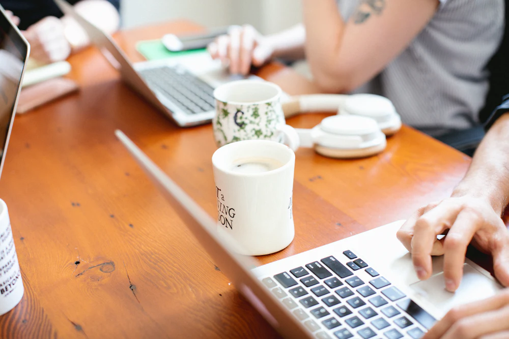 People working together at a wooden table with laptops and mugs of coffee
