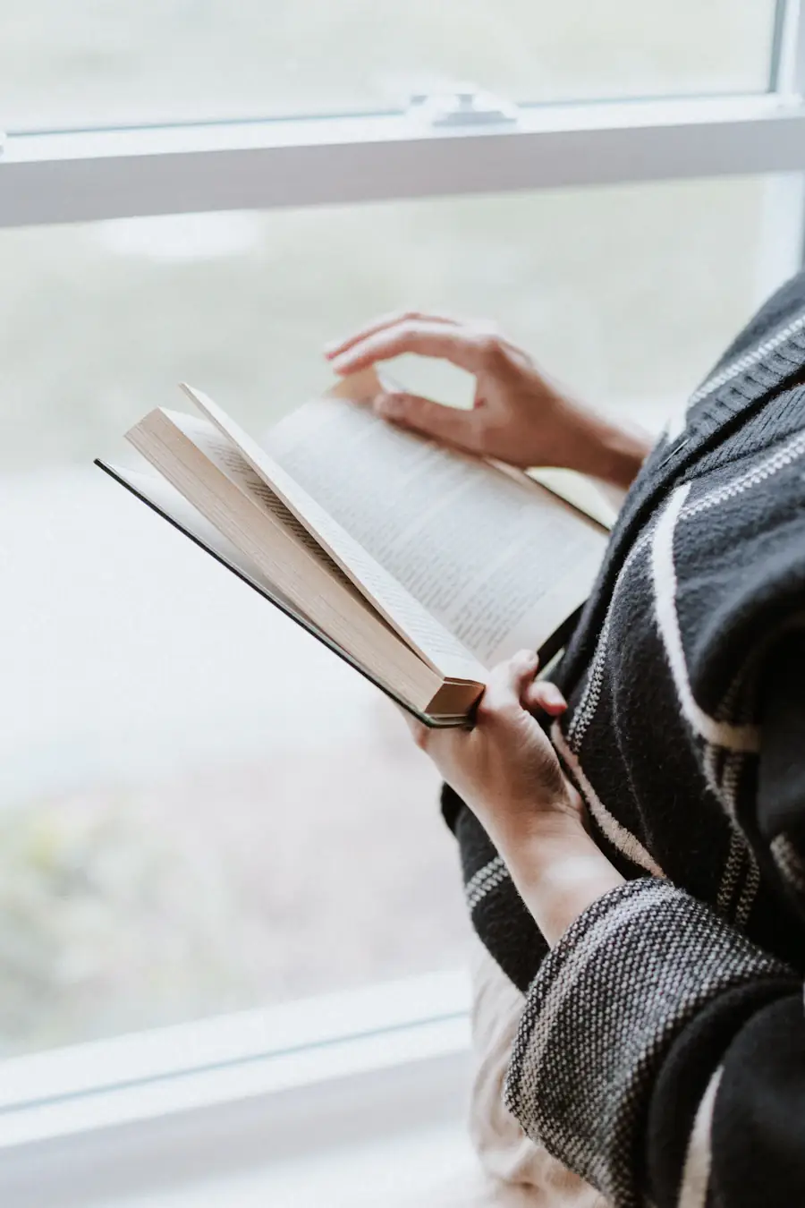 A person reading a book beside a window