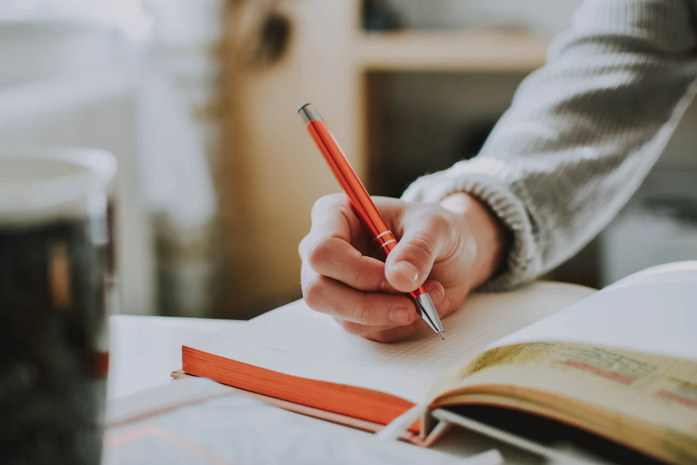 A hand writing in a notebook beside an open book